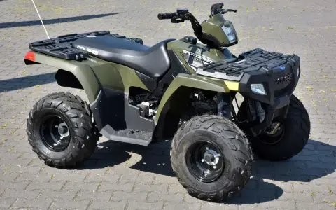 Zielony quad Polaris Sportsman 300 na kostce brukowej.