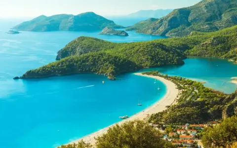 Turcja zachwyca turkusowym morzem i zielonymi wzgórzami. Widok na zatokę z plażą i górami.