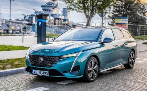 Turkusowe kombi Peugeot 308 zaparkowane na bruku, w tle okręt wojenny.