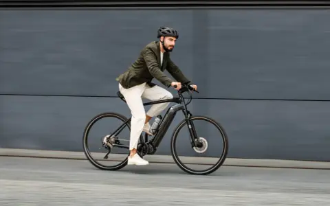 Mężczyzna w kasku i marynarce jedzie na rowerze elektrycznym po szarym tle.