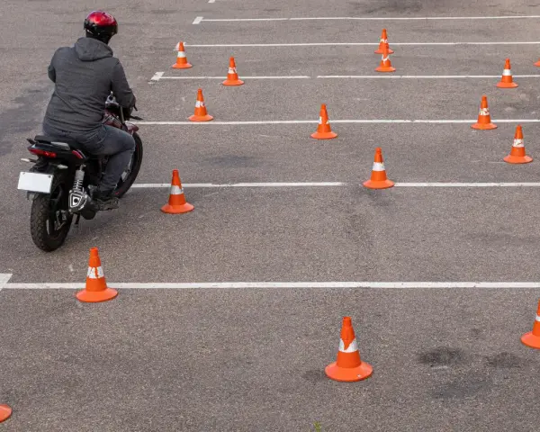 Motocyklista w kasku pokonuje tor przeszkód z pachołków, ćwicząc jazdę na prawo jazdy **kategoria a2**.