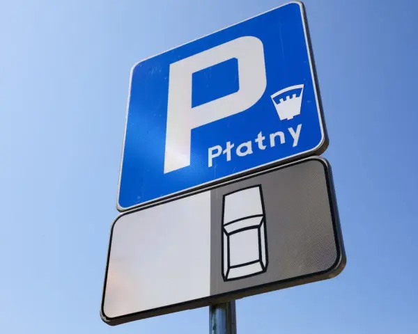 Znak D18 informuje o płatnym parkingu. Widoczny symbol samochodu sugeruje miejsce postojowe.