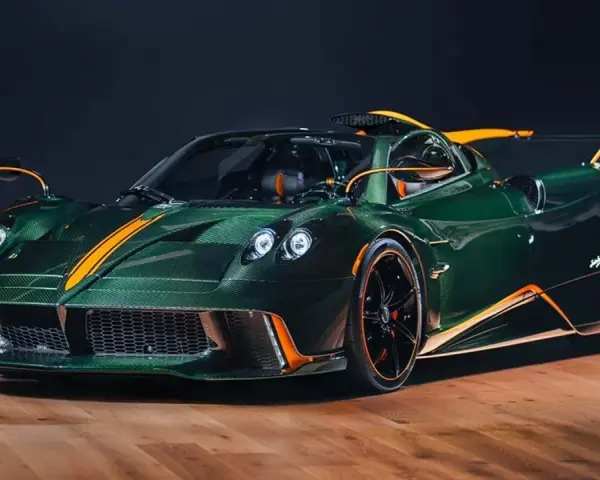 Pagani Huayra w kolorze głębokiej zieleni z pomarańczowymi akcentami, prezentuje swoje karbonowe nadwozie na drewnianej podłodze.