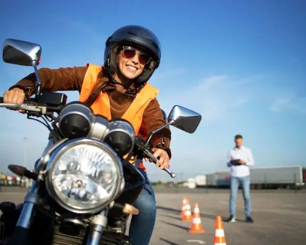 Uśmiechnięta kobieta w kasku i kamizelce na motocyklu, przygotowuje się do egzaminu na prawo jazdy na motor.