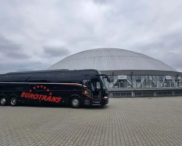 Czarny autokar turystyczny "Eurotrans" przed nowoczesnym budynkiem z kopułą.