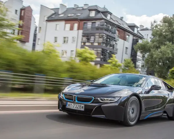 Czarny BMW i8 pędzi ulicą, mijając nowoczesne budynki i zielone drzewa.