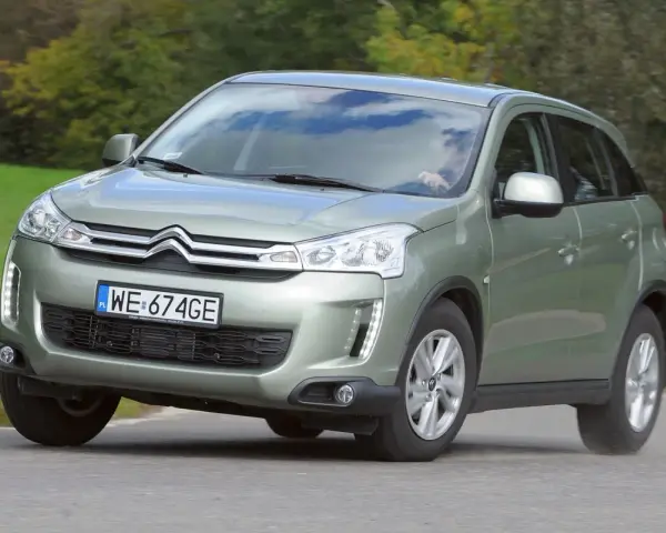 Zielony Citroën C4 Aircross z polskimi tablicami WE 674GE jedzie po drodze wśród zieleni.