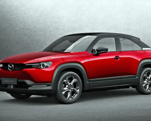 Czerwona Mazda MX-30 z czarnym dachem prezentuje się stylowo na tle szarej ściany.
