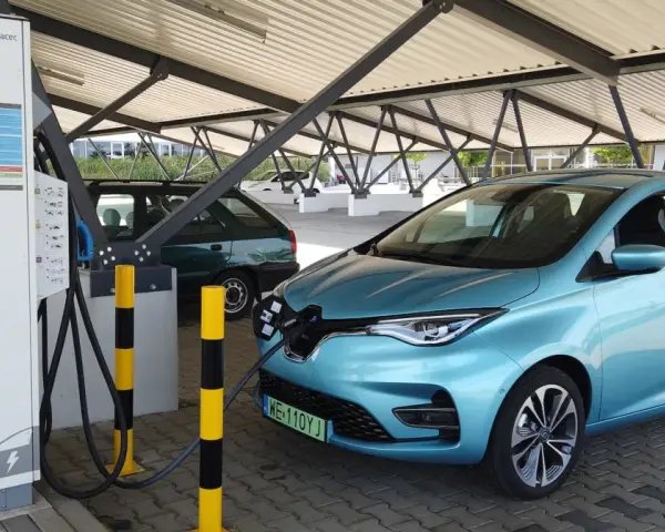 Błękitny Renault Zoe podłączony do ładowarki na parkingu pod zadaszeniem.