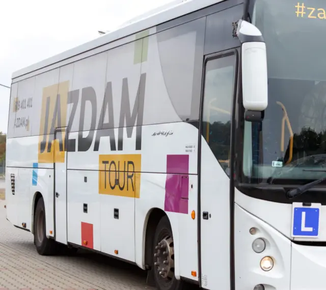 Biały autokar z napisem "JAZDAM TOUR" i hasłem "#zapierw". Kierowca macha. Zastanawiasz się, ile kosztuje autobus?
