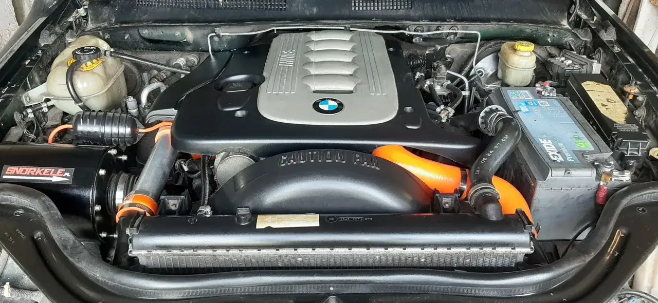 Silnik BMW m57 z zamontowanym snorkel'em i pomarańczowymi wężami. Widać akumulator Exide i chłodnicę.