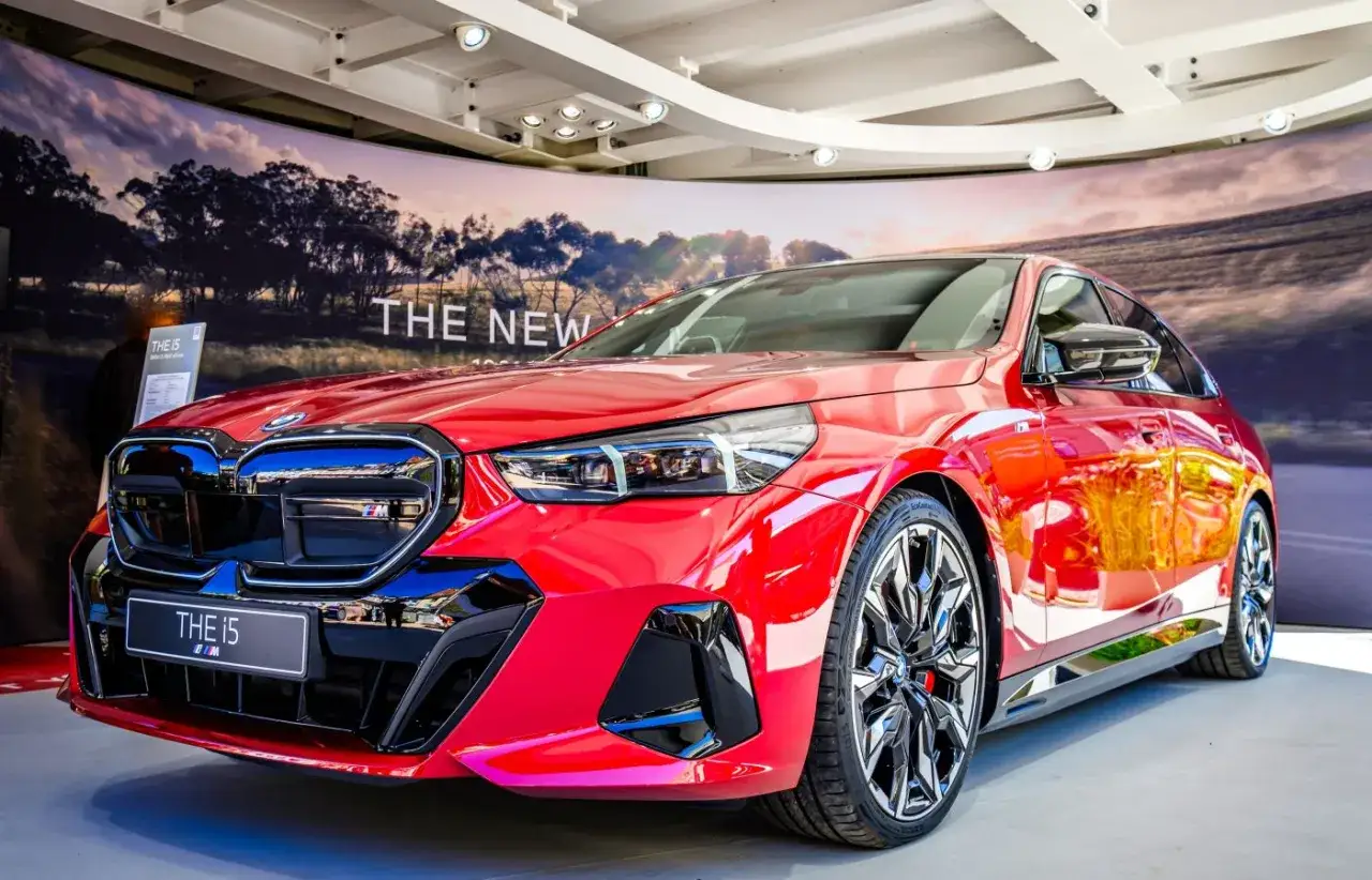 Błyszczące, czerwone BMW i5 prezentuje się imponująco na tle krajobrazu.