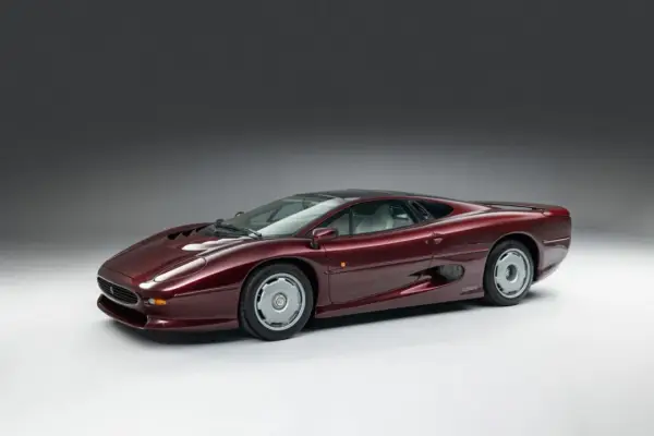 Bordowy Jaguar XJ220, ikona motoryzacji lat 90., prezentuje swoje aerodynamiczne linie na tle szarego tła.