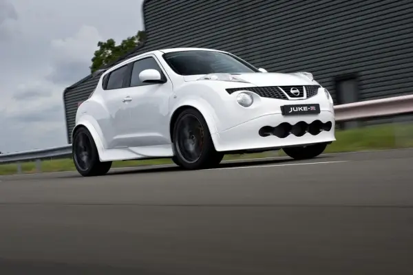 Biały Nissan Juke-R pędzi po torze, jego sportowy wygląd podkreślają szerokie nadkola i agresywny przedni zderzak.