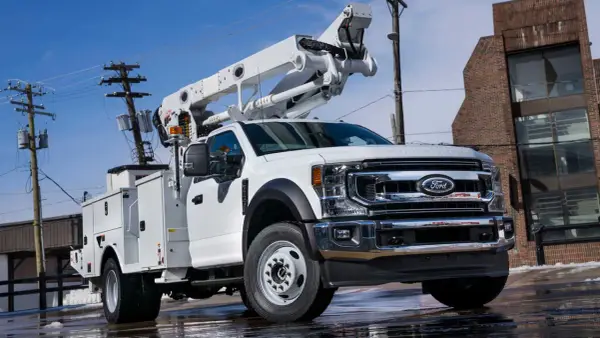 Biały Ford F650 z podnośnikiem koszowym gotowy do pracy przy liniach energetycznych.