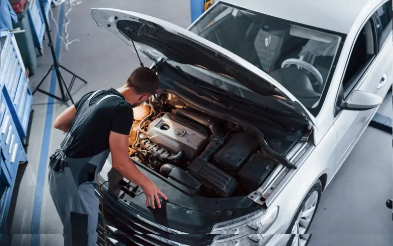 Młody mechanik w kombinezonie pracuje przy silniku białego samochodu. To jego pasja, każdy konstruktor marzy o takiej precyzji.