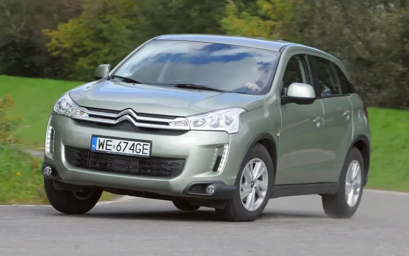 Zielony Citroën C4 Aircross z polskimi tablicami WE 674GE jedzie po drodze wśród zieleni.