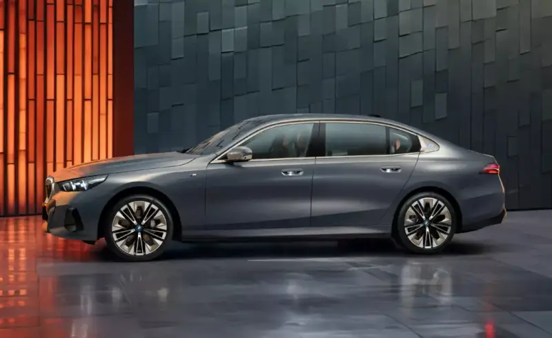 Eleganckie, szare BMW i5 z niebieskim akcentem na błotniku, prezentujące się na tle nowoczesnej, geometrycznej ściany.